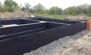 Fundament domu z izolacją przeciwwilgociową. Czarna masa bitumiczna chroni ściany przed wilgocią, a drenażowa membrana zapobiega gromadzeniu się wody.