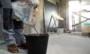 Budowlaniec wsypuje zaprawę do wiadra, przygotowując się do wylewki na styropian. Kluczowe jest dobranie odpowiedniej grubości wylewki, np. ile cm wylewki na styropian.