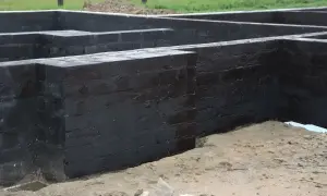 Fundament z czarnej cegły, przygotowany do izolacji. Widać, że prace postępują, a fundamenty są już prawie gotowe, co pozwala disprobit na dalsze etapy budowy.