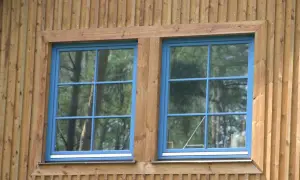Dwa niebieskie okna z ozdobnymi szprosami do okien, osadzone w drewnianej elewacji.