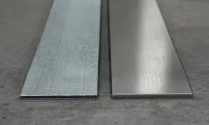 Dwa metalowe paski leżą obok siebie na betonowym podłożu. Jeden jest szorstki, drugi gładki, jakby przygotowany do montażu kotwy.