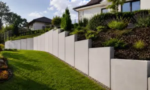 Nowoczesny, betonowy mur oporowy pięknie komponuje się z zielonym trawnikiem i zadbanym ogrodem.