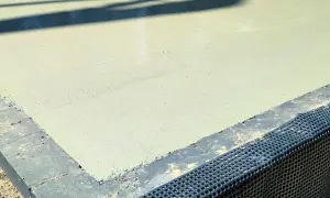 Świeżo wylany beton na budowie. Powierzchnia jest gładka, a cień rzucany przez coś na górze przypomina chudziaka.