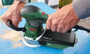 Ręce trzymają zieloną szlifierkę Bosch PEX 400 AE, która jest idealna do szlifowania gipsu.