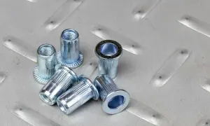 Kilka metalowych nitonakrętek leży na chropowatej, metalowej powierzchni.