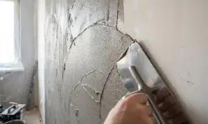 Ręka z kielnią rozprowadza gładką masę gipsową na ścianie, przygotowując ją do malowania.