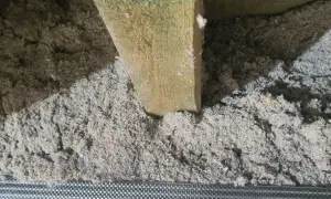Luźna, szara celuloza wypełnia przestrzeń między drewnianymi belkami, tworząc izolację.