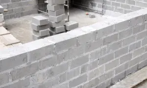 Budowa fundamentów z bloczków betonowych. Stos świeżo ułożonych bloczków betonowych fundamentowych obok wznoszonej ściany.