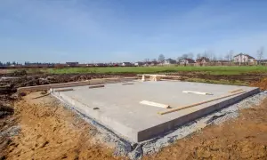 Płyta fundamentowa, jeden z rodzajów fundamentów, gotowa pod budowę domu. W tle widać domy i zielone pola.