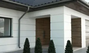 Nowoczesny dom z białymi boniami, drewnianymi drzwiami i czarnym dachem.