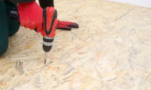 Ręka w czerwonej rękawicy wkręca wkręt w suchy jastrych z płyt OSB.