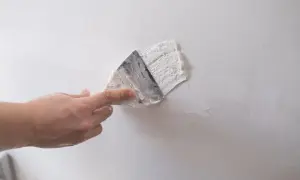 Dłoń zacierająca gips szpachlowy na białej ścianie. Czas, ile schnie gips szpachlowy, zależy od warunków.