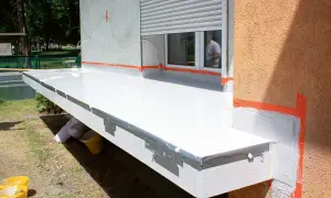 Trwa remont balkonu. Nowa, biała posadzka lśni, a pomarańczowa taśma zabezpiecza krawędzie.