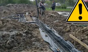 Budowa fundamentów: betonowanie zbrojenia w wykopie, obok żółty znak ostrzegawczy.