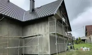 Dom w trakcie prac elewacyjnych. Rusztowanie wokół budynku, szara ściana. Sprawdź elewacja cena za m2 robocizna.