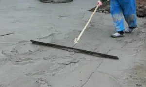 Robotnik w niebieskich spodniach wyrównuje świeżą wylewkę miksokretem.