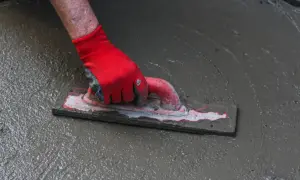 Dłoń w czerwnej rękawicy wygładza mokrą wylewkę pacą.