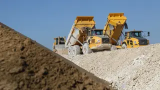 Żółte wywrotki pracują na budowie, tworząc imponujący kompozyt maszyn i ziemi pod błękitnym niebem.