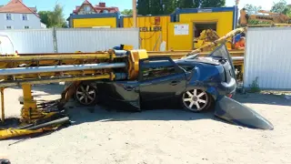 Zniszczony samochód pod ciężką palownicą na placu budowy.