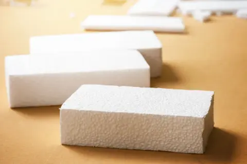 Białe bloki styropianu na brązowym tle. Czy styropian pije wodę? Ten materiał jest lekki i porowaty, ale nie wchłania wilgoci.