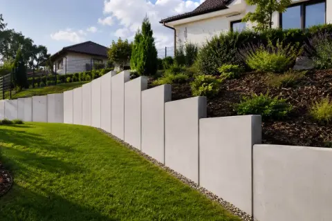 Nowoczesny, betonowy mur oporowy pięknie komponuje się z zielonym trawnikiem i zadbanym ogrodem.