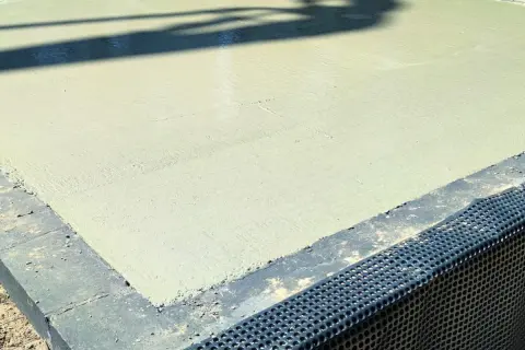 Świeżo wylany beton na budowie. Powierzchnia jest gładka, a cień rzucany przez coś na górze przypomina chudziaka.