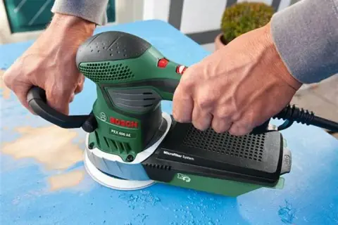 Ręce trzymają zieloną szlifierkę Bosch PEX 400 AE, która jest idealna do szlifowania gipsu.