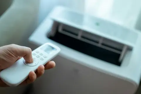 Dłoń trzymająca pilot do klimatyzatora bez jednostki zewnętrznej. Urządzenie chłodzi pomieszczenie.