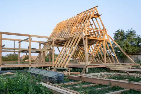 Drewniana konstrukcja domku letniskowego w budowie. Widać szkielet dachu i ścian, a także elementy, które mogą stanowić jaki fundament pod domek letniskowy drewniany.