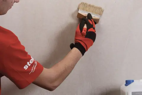 Gruntowanie płyt karton gips to kluczowy etap przygotowania powierzchni. Ręka w rękawicy nakłada preparat pędzlem na ścianę.