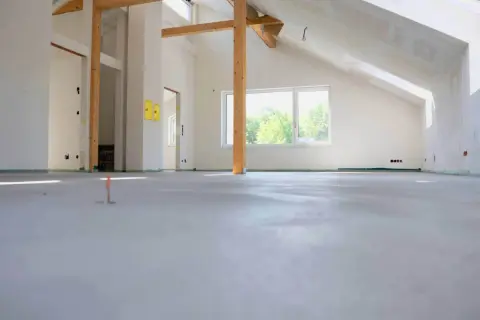 Nowe wnętrze z drewnianymi belkami i oknem. Podłoga gotowa pod wykończenie, zastanawiasz się, ile za metr wylewki?