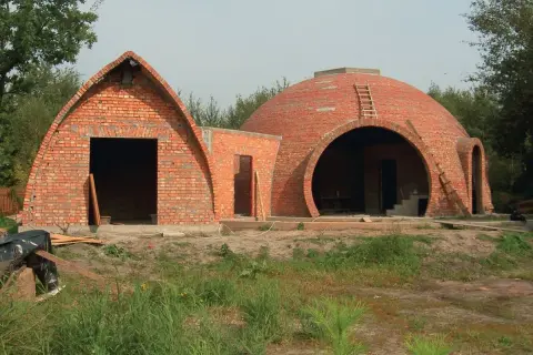 Dwa budynki z cegły, jeden z łukowatym dachem, drugi z okrągłą kopułą, w trakcie budowy.