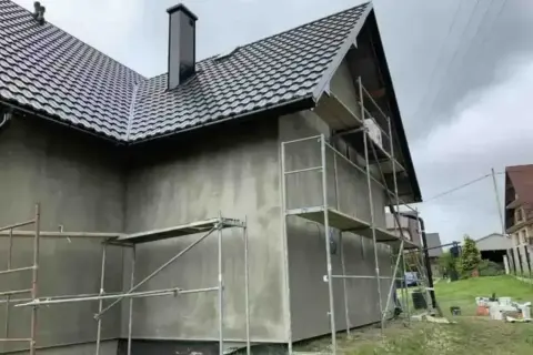 Dom w trakcie prac elewacyjnych. Rusztowanie wokół budynku, szara ściana. Sprawdź elewacja cena za m2 robocizna.