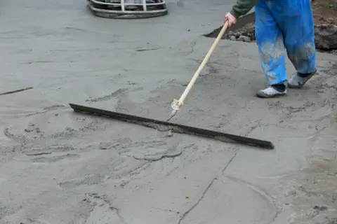Robotnik w niebieskich spodniach wyrównuje świeżą wylewkę miksokretem.