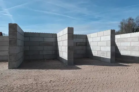 Budowa muru oporowego z bloczków betonowych. Zbrojenie widoczne na górze ścian.