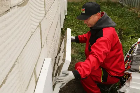 Budowlaniec w czerwonym stroju montuje płyty styropianowe na ścianie fundamentowej, zastanawiając się, jakiej grubości styrodur na fundamenty będzie najlepszy.