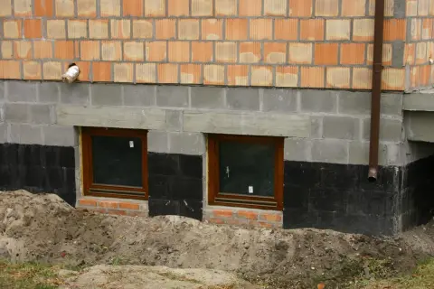 Budowa fundamentu pod starym domem: widok na ściany z pustaków, okna piwniczne i izolację przeciwwilgociową.