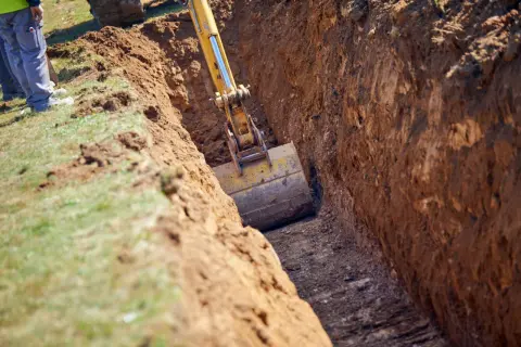 Koparka pogłębia wykop, pokazując, jak głęboko fundamenty będą sięgać. Pracownicy obserwują postęp prac.