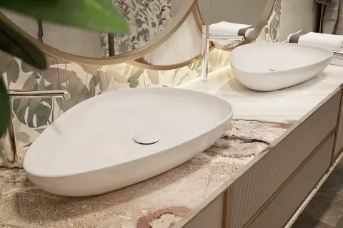 Elegancka łazienka z dwiema owalnymi umywalkami na blacie z konglomeratu. W tle lustro i tropikalna tapeta.