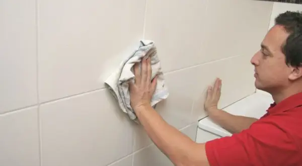 Mężczyzna czyści białe płytki na ścianie łazienki, pokazując, jak wyczyścić fugi na ścianie.