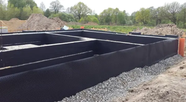 Fundament domu z izolacją przeciwwilgociową. Czarna masa bitumiczna chroni ściany przed wilgocią, a drenażowa membrana zapobiega gromadzeniu się wody.