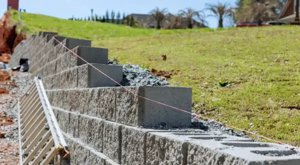 Budowa muru oporowego z betonowych bloków, z drabiną i sznurkiem do poziomowania. Kara za mur oporowy? Nie, to inwestycja w stabilność skarpy.