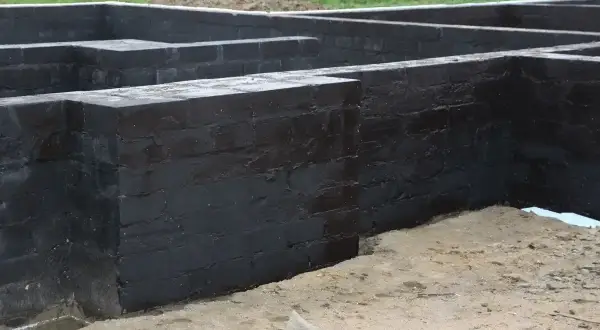 Fundament z czarnej cegły, przygotowany do izolacji. Widać, że prace postępują, a fundamenty są już prawie gotowe, co pozwala disprobit na dalsze etapy budowy.