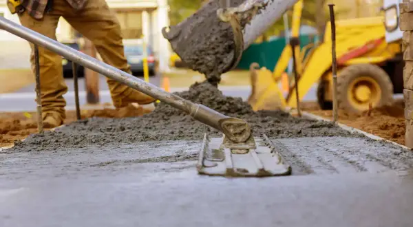 Pracownik wylewa beton, który można lać do temperatury ok. 30°C. W tle koparka.