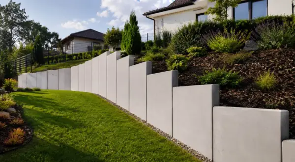 Nowoczesny, betonowy mur oporowy pięknie komponuje się z zielonym trawnikiem i zadbanym ogrodem.