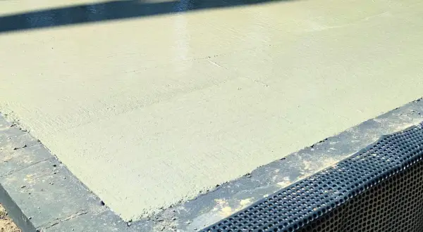Świeżo wylany beton na budowie. Powierzchnia jest gładka, a cień rzucany przez coś na górze przypomina chudziaka.