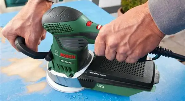 Ręce trzymają zieloną szlifierkę Bosch PEX 400 AE, która jest idealna do szlifowania gipsu.
