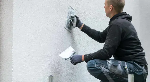 Mężczyzna nakłada tynk dekoracyjny z gipsu na ścianę, tworząc teksturę.