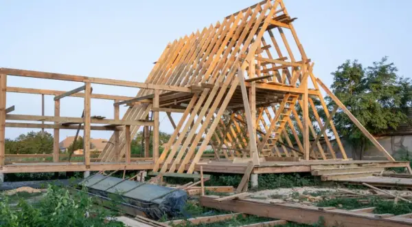 Drewniana konstrukcja domku letniskowego w budowie. Widać szkielet dachu i ścian, a także elementy, które mogą stanowić jaki fundament pod domek letniskowy drewniany.