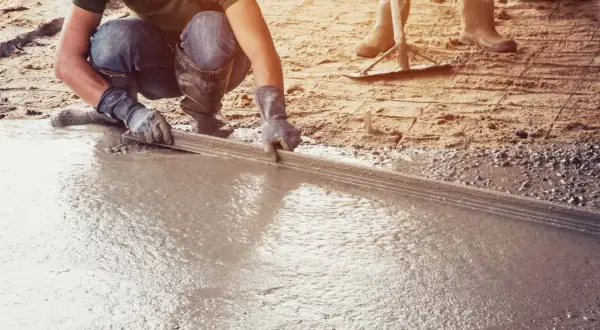 Pracownik wyrównuje świeżą wylewkę betonową na ziemi za pomocą łaty. To kluczowy etap, jak zrobić wylewkę betonową na ziemi.